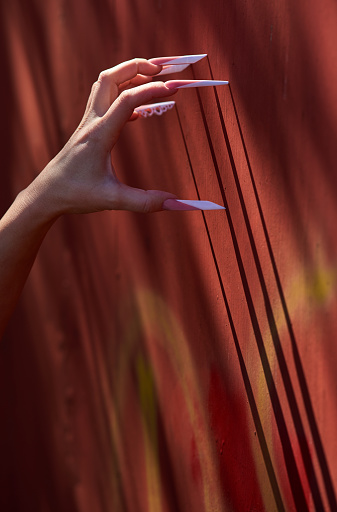 vertical shot of angry woman hand with long artificial nails scratching the wall.side view.