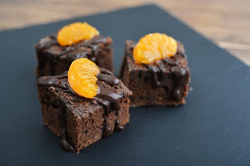 Homemade chocolate brownies with fresh oranges on black slate background