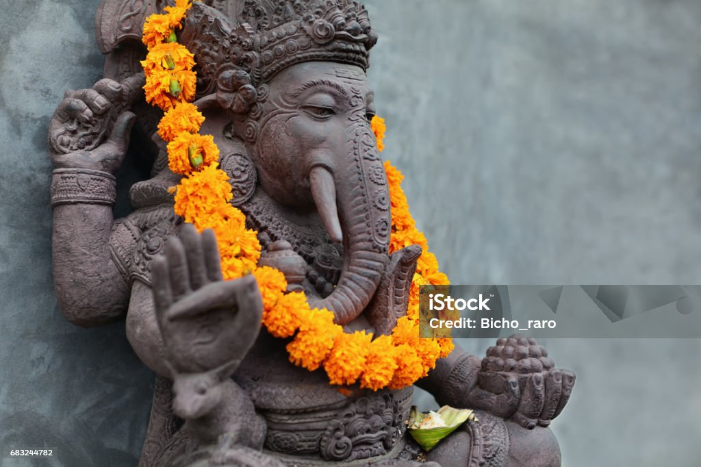 Ganesha with balinese Barong masks, flowers necklace and ceremonial offering Ganesha with balinese Barong masks sitting on front of temple. Decorated for religious festival by orange flowers necklace and ceremonial offering. Travel background, Bali island art and culture. Bali Stock Photo