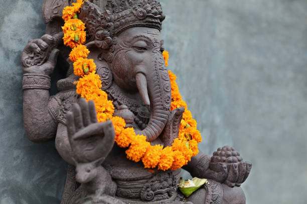 Ganesha with balinese Barong masks, flowers necklace and ceremonial offering Ganesha with balinese Barong masks sitting on front of temple. Decorated for religious festival by orange flowers necklace and ceremonial offering. Travel background, Bali island art and culture. hindu ganesh mask stock pictures, royalty-free photos & images
