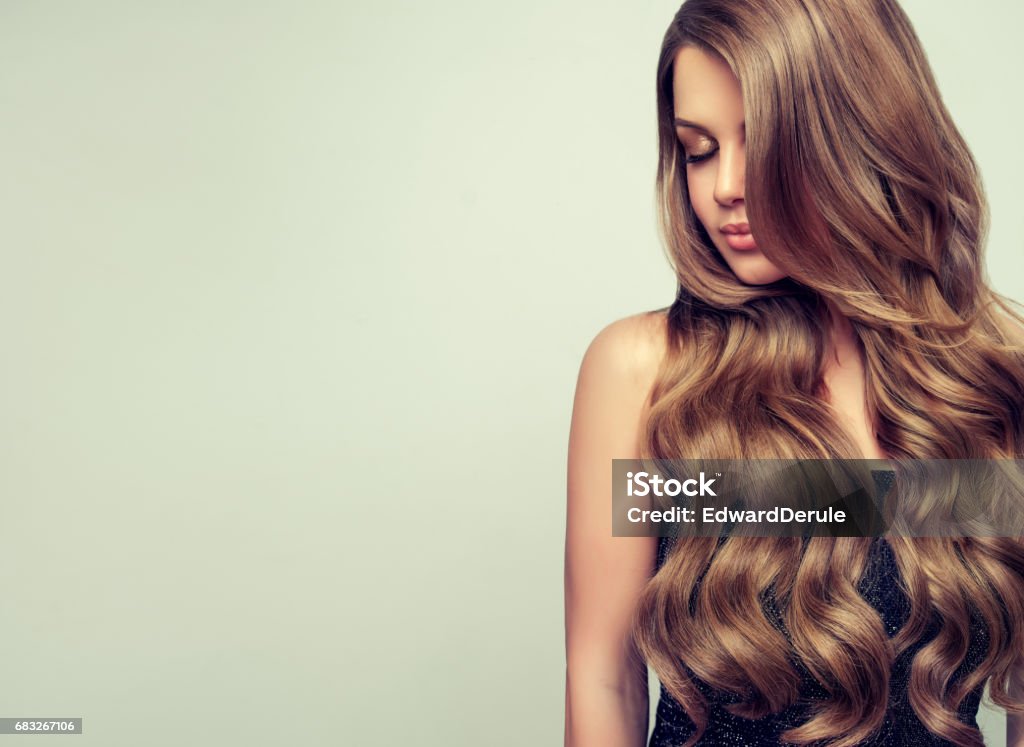 Portrait of gorgeous young woman with elegant make up and perfect hairstyle. Long haired, appealing model with dense, curled, well cared hair. Portrait of gorgeous young woman with elegant make up and perfect hairstyle. Straight look at camera. Long Hair Stock Photo