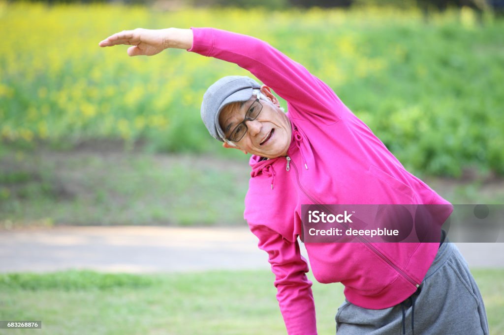 senior Japanese man in pink wear doing standing side bend exercise portrait of senior Japanese man in pink wear doing standing side bend exercise on a lawn Artistic Gymnastics Stock Photo