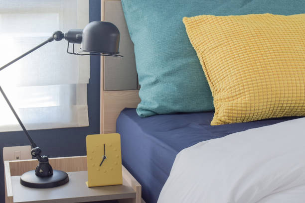istock Yellow modern clock on bedside table with colorful pillows in background 683294040