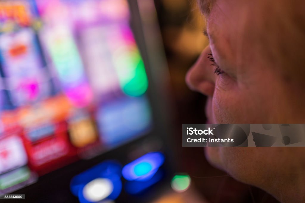 Una donna matura, seduta di fronte a una slot machine, sta seriamente controllando lo schermo mentre scommette in un casinò di Las Vegas. - Foto stock royalty-free di Donne mature