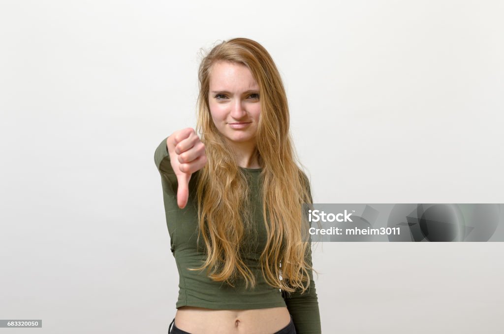 Rebellious negative woman giving a thumbs down Rebellious negative woman giving a thumbs down gesture with a frown to show her displeasure and register a no vote Adult Stock Photo