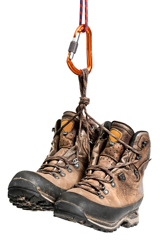 Used hiking boots hanging from a carabiner, isolated on a white background.