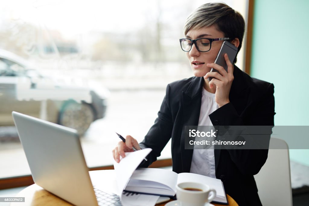 Busy broker Busy young woman consulting client ahile planning work in cafe Using Phone Stock Photo