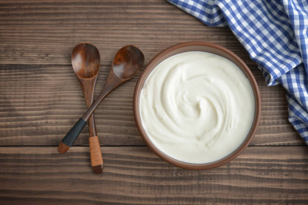 Yogurt in bowl Yogurt in bowl with spoon on wooden background, top view cream dairy product stock pictures, royalty-free photos & images