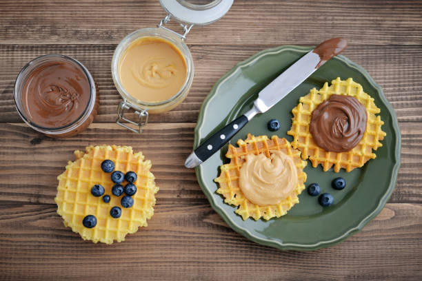Belgian waffles with chocolate cream and peanut butter on wooden background, top view