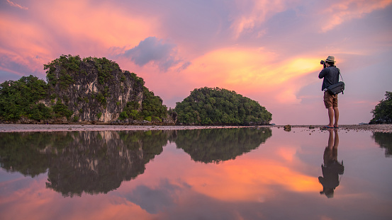 Reflection of man photographer take photo of summer landscape with beautiful sunset sky at Ao Nang Beach, famous tourist attraction and travel destination of Krabi Province, Thailand