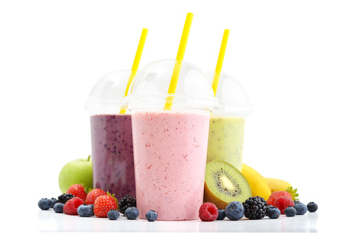 Fruit smoothies in plastic cups with blueberry, strawberry, kiwi, blackberry, raspberry and banana isolated on white background. Take away drinks concept.