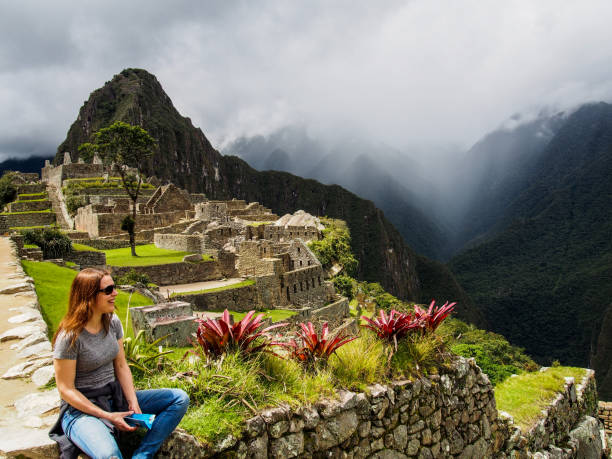 Happy Moments at the Ancient Lost City Cheerful Woman Sitting at Ancient Stone and Looking at Machu Picchu Mountains peru travel stock pictures, royalty-free photos & images