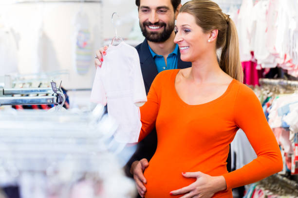 donna incinta e uomo che comprano vestiti per bambini in negozio - human pregnancy clothing shopping retail foto e immagini stock