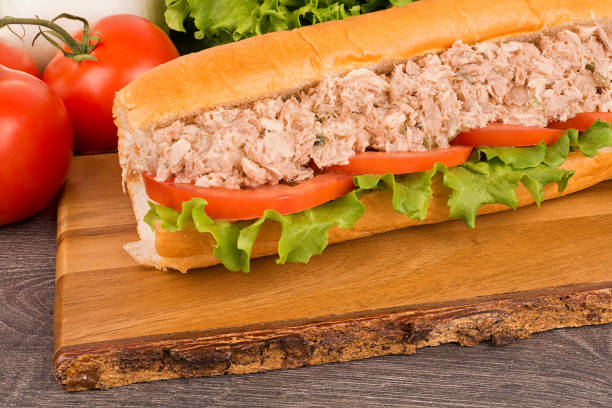 Close up on submarine tuna sandwich, vegetables in background. Close up on submarine tuna salad sandwich, vegetables in background. tuna salad sub stock pictures, royalty-free photos & images