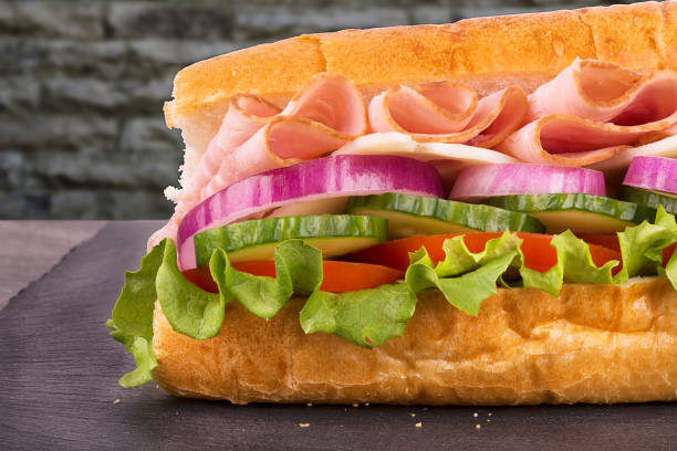 istock Close up on submarine ham sandwich, brick wall in background. 683398688