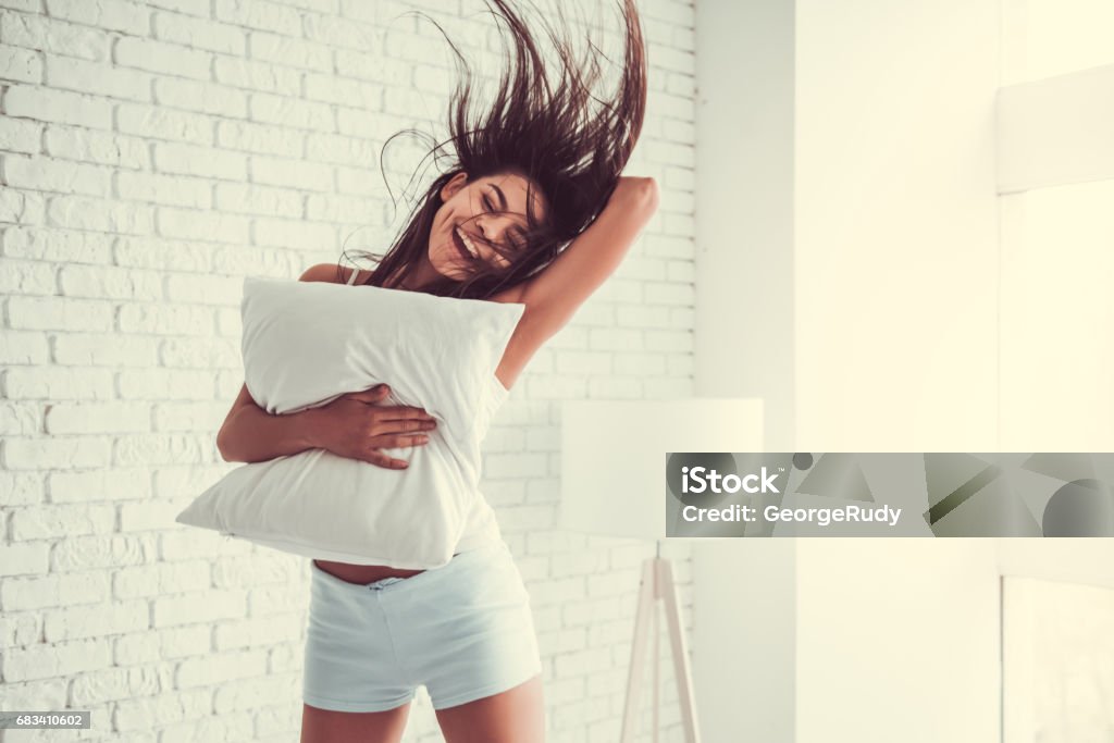 Girl in the bedroom Happy young beautiful woman jumping on the bed at home, hugging pillow. Women Stock Photo