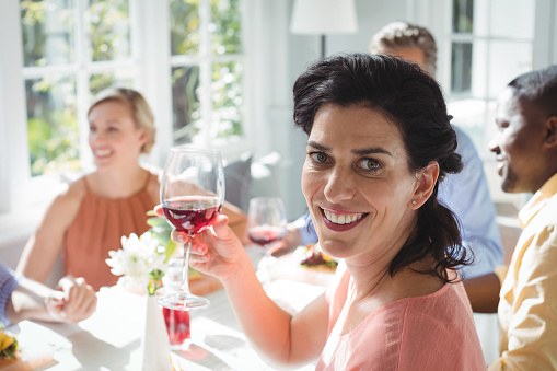 Smiling woman holding glass of red wine at dining table