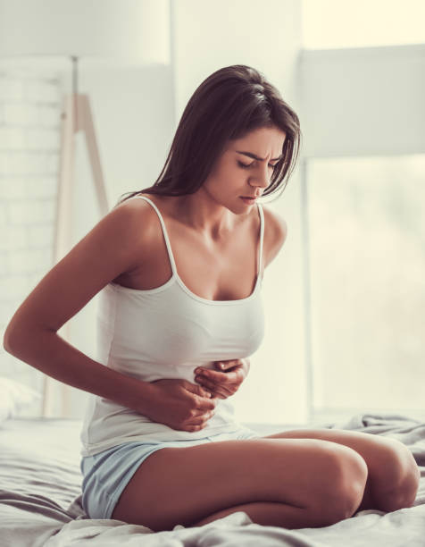 Girl in the bedroom Young woman suffering from abdominal pain while sitting on bed at home headache menstruation pain cramp stock pictures, royalty-free photos & images