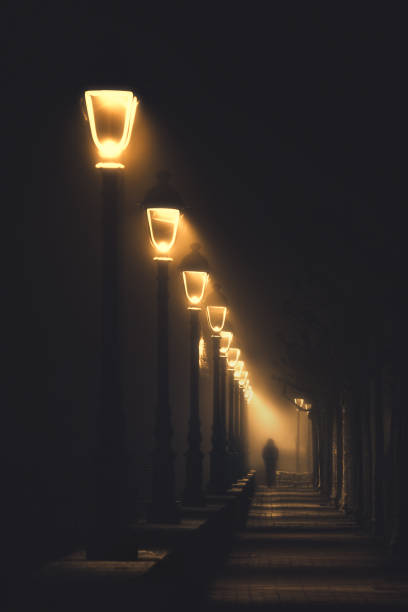 persona caminando en la calle oscura iluminada con farolas - narrow alley fotografías e imágenes de stock