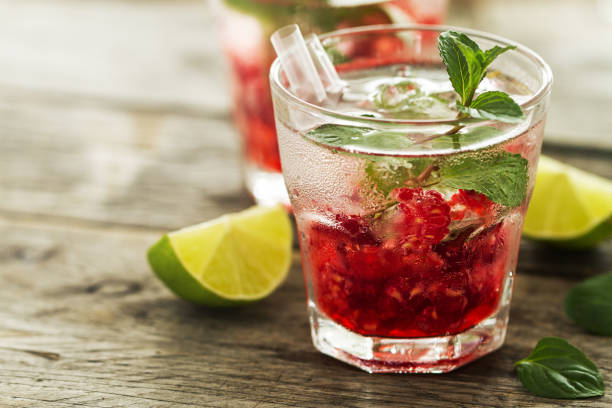 tasty cold fresh drink lemonade with raspberry, mint, ice and lime in glass on wooden background. closeup. - water with glass cocktail imagens e fotografias de stock