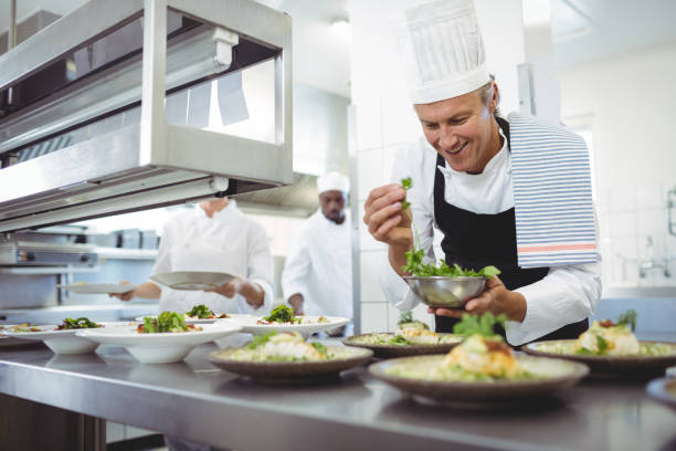 Happy chef garnishing appetizer plates at order station in restaurant