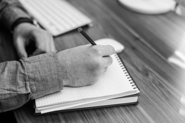 istock black and white image of hand writing in notebook on wooden table 683461776