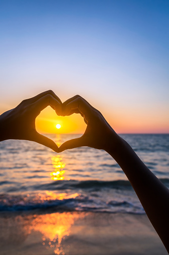 female hands in heart shape on sea beach at sunset background, Summer season