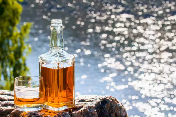 Bottle and a glass of whiskey on a rock above the river