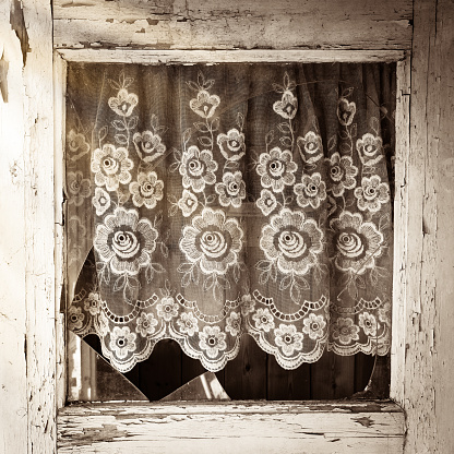 Close up of old house door window frame with broken glass and with white flower pattern curtain