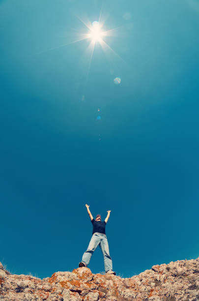 hombre joven en jeans y camisa negra en una montaña levantó sus manos al cielo hacia el sol. - on top of business cliff businessman fotografías e imágenes de stock