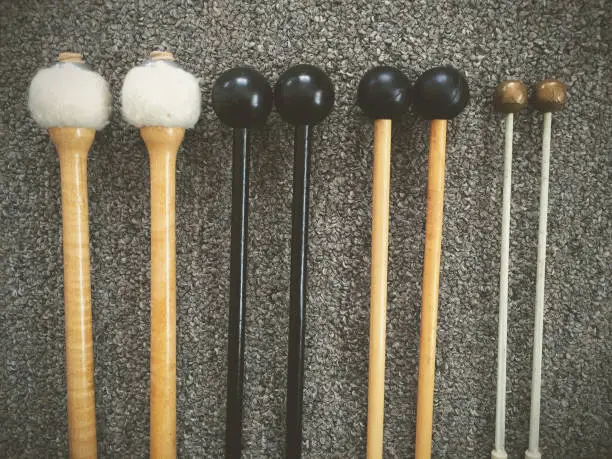 Assorted percussion mallets lined up, for playing timpani, xylophone, marimba, and glockenspiel
