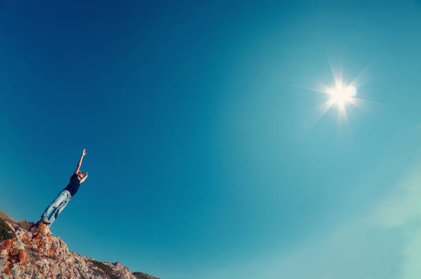jeune homme en jeans et chemise noire sur une montagne déclenché leurs mains vers le ciel vers le soleil - on top of business cliff businessman photos et images de collection