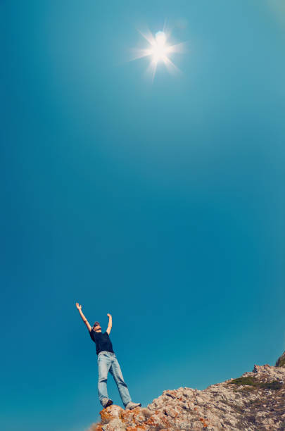 hombre joven en jeans y camisa negra en una montaña levantó sus manos al cielo hacia el sol. - on top of business cliff businessman fotografías e imágenes de stock