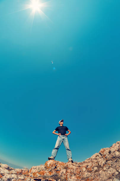 jeune homme en jeans et chemise noire sur un rocher de montagne en levant vers le ciel - on top of business cliff businessman photos et images de collection