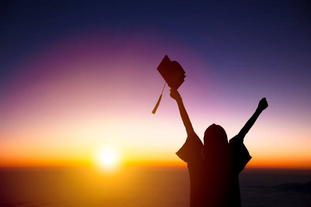 silhouette di studente che celebra la laurea guardando la luce del sole - woman with arms raised back view foto e immagini stock