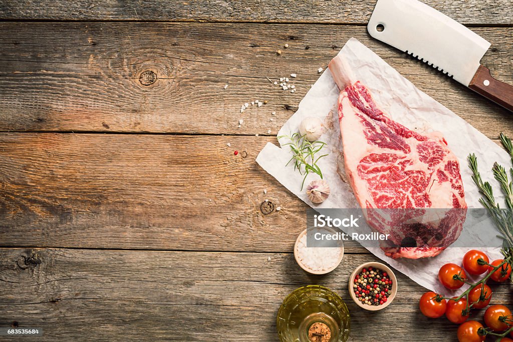 Raw tomahawk beef steak Raw tomahawk beef steak with ingredients for grilling: seasoning, fresh rosemary and olive oil on wooden background, top view Angle Stock Photo