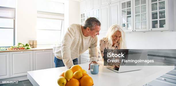 Senior Couple Relaxing In A Kitchen With A Laptop Stock Photo - Download Image Now - Couple - Relationship, Senior Couple, Kitchen