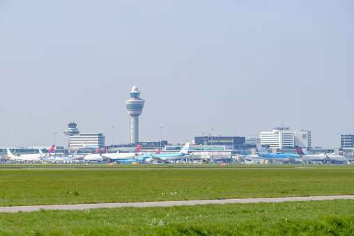 Amsterdam Airport Schiphol (AMS) international hub main international airport of the Netherlands. Airplanes are waiting at the gate and taxxiing to the runways with the Schiphol air traffic control tower in the background.