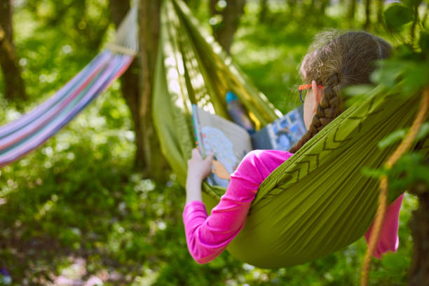 uma garota numa rede é ler um livro em copos. - hammock comfortable lifestyles relaxation - fotografias e filmes do acervo