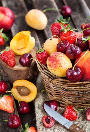 Fresh ripe summer berries and fruits (peaches, apricots, cherry and strawberry) in wicker basket