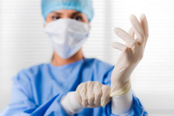 female doctor surgeon putting on surgical gloves - luva peça de roupa imagens e fotografias de stock