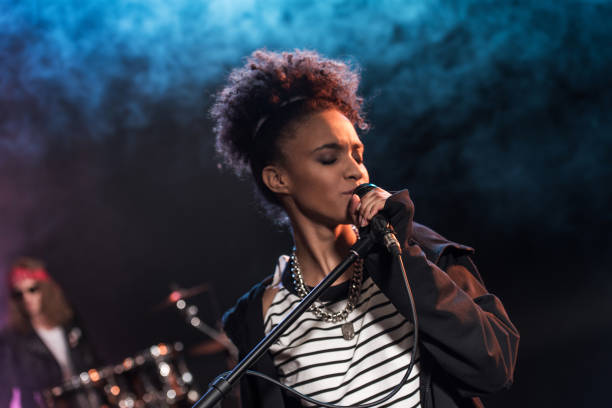 cantante femenina con micrófono y rock and roll band interpretando música de rock duro en el escenario - musical band fotografías e imágenes de stock