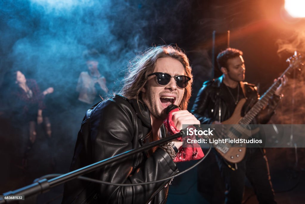 Male singer with microphone and rock and roll band performing hard rock music on stage Rock Music Stock Photo