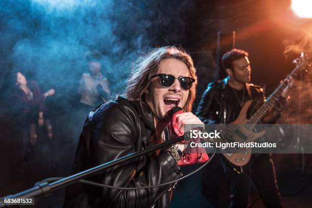 Male Singer With Microphone And Rock And Roll Band Performing Hard Rock Music On Stage Stock Photo - Download Image Now