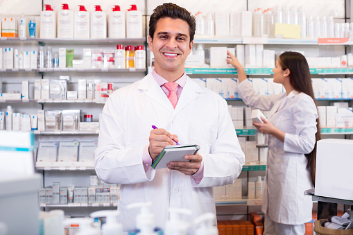Smiling pharmacist and pharmacy technician posing in pharmacy