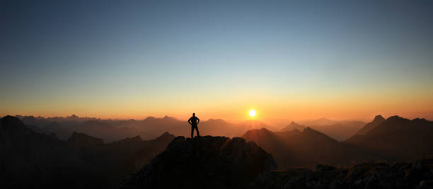 istock Man reaching summit enjoying freedom and looking towards mountains sunset. 683726056