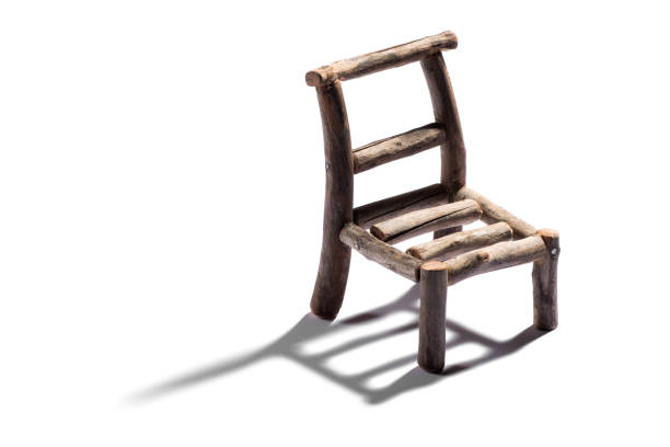 Small rustic handmade model of a chair made from rough wood casting a shadow across a white background with copy space