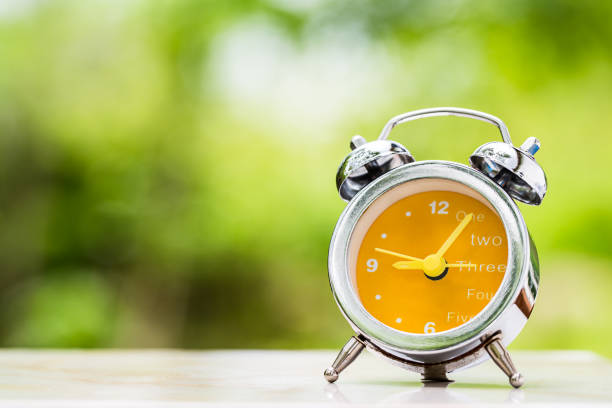 istock retro clock on wooden table over blurred spring garden 683736518