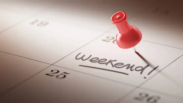 Concept image of a Calendar with a red push pin. Closeup shot of a thumbtack attached. The words Weekend written on a white notebook to remind you an important appointment.