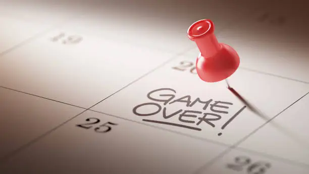 Concept image of a Calendar with a red push pin. Closeup shot of a thumbtack attached. The words Game over written on a white notebook to remind you an important appointment.